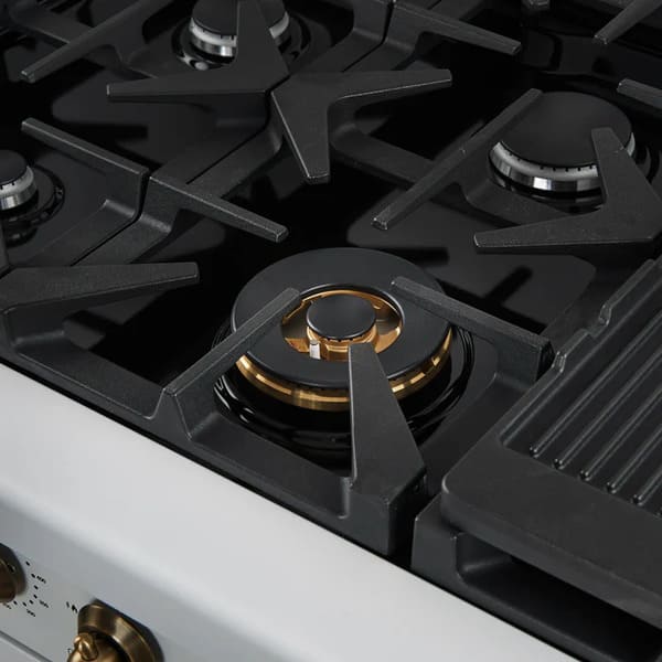 Close-up of a brass burner on the Forno Antico 48-Inch Gas Range in white, highlighting the precision flame ports, durable cast iron grate, and elegant matte white cooktop surface.